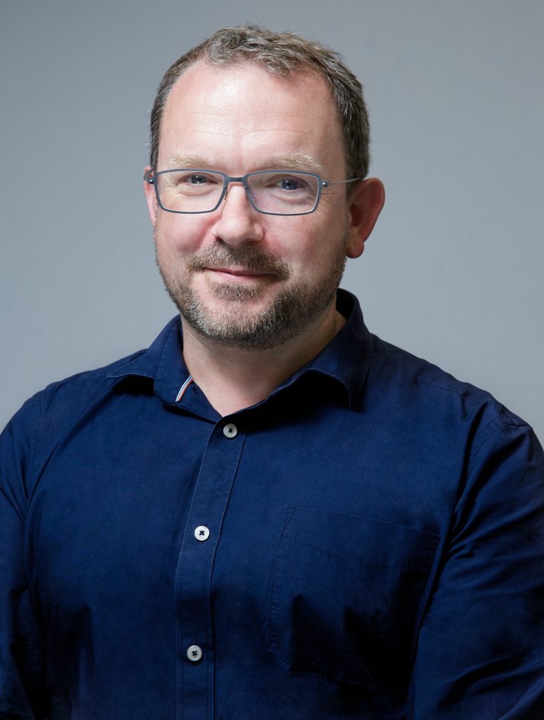 A portrait image of Ben Sowter, Senior Vice President of QS, smiling and looking at the camera. Mr Sowter is wearing glasses and a navy shirt.